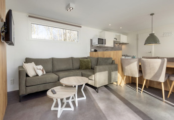 Stue i Chalet Comfort 6 ved Hunzepark, Nederlandene, med moderne sofa, spisebord og åbent køkken.