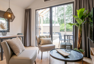 Soggiorno moderno nel Tiny House 2 con ampie finestre, arredo accogliente e vista bosco a Bospark 't Wolfsven.