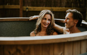 A middle-aged couple relaxes in a wooden hot tub at Luxe bosrand loft, Si-Es-An Campsite, Netherlands.