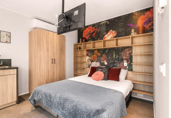 Chambre moderne avec lit double, fresque murale, TV suspendue et kitchenette dans une maison nature aux Pays-Bas.