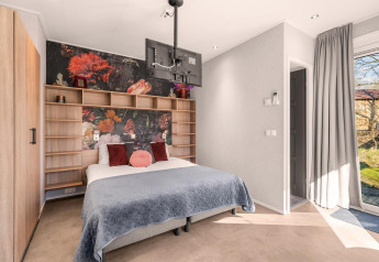 Dormitorio moderno con mural floral, cama doble, estantes de madera y TV colgado en un espacio luminoso.
