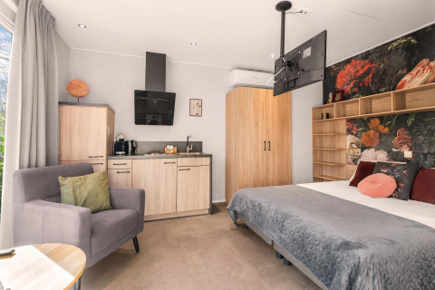 Estudio moderno con cocina, sillón, cama y mural floral en el camping Si-Es-An, Países Bajos.