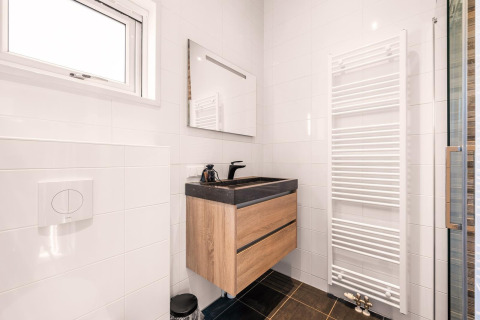 Bagno moderno con mobile in legno, lavabo nero, grande specchio e scaldasalviette in una Nature House.