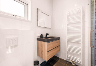 Moderne badkamer met houten meubel, zwarte wasbak, spiegel en verwarmd handdoekenrek in Nature House.