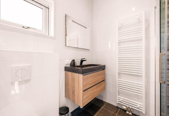 Salle de bain moderne avec meuble en bois, lavabo noir, grand miroir et porte-serviettes chauffant.