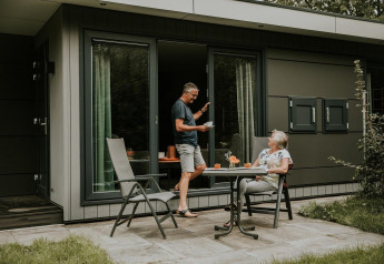 Un couple âgé prend un café devant une maison nature moderne sur un camping aux Pays-Bas.