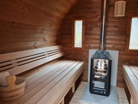 Vista interior de una sauna de madera con bancos, estufa y cubeta en una casa natural en Holanda.