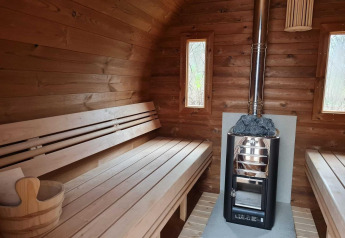 Binnenaanzicht van een houten sauna met bankjes, kachel en emmer in een natuurhuisje in Nederland.