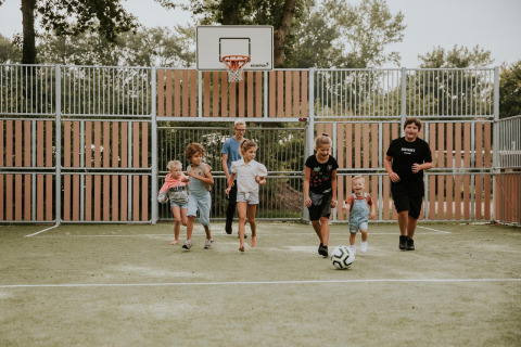 Kinderen en een volwassene spelen voetbal op een veld bij Luxe bosrand loft, camping Si-Es-An, Nederland.