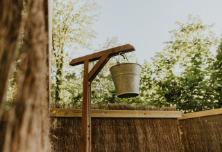 Metalen emmer hangend aan houten frame buiten, omringd door bomen bij camping Si-Es-An, Nederland.
