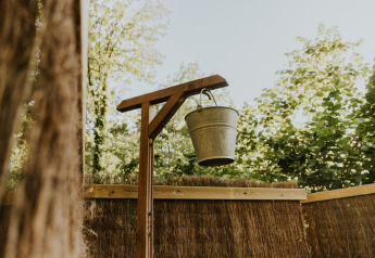 Cubo de metal colgado de un marco de madera al aire libre, rodeado de árboles en Si-Es-An, Holanda.