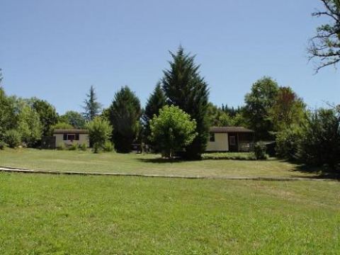 Groot grasveld met bomen en twee kleine huisjes in Domaine Papillon vakantiepark in Occitanië, Frankrijk.
