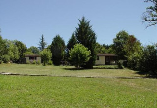Groot grasveld met bomen en twee kleine huisjes in Domaine Papillon vakantiepark in Occitanië, Frankrijk.