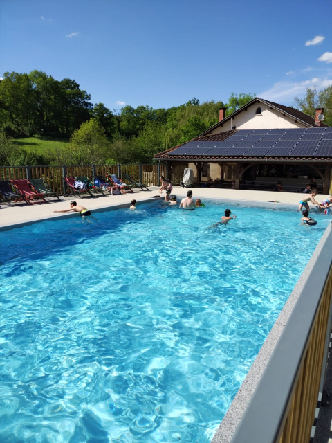Buitenzwembad met mensen, ligstoelen en huis met zonnepanelen bij Domaine Papillon, Occitanie, Frankrijk.