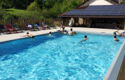 Buitenzwembad met mensen, ligstoelen en huis met zonnepanelen bij Domaine Papillon, Occitanie, Frankrijk.