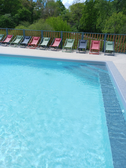 Buitenzwembad met helderblauw water en kleurrijke ligstoelen bij Domaine Papillon in Occitanië, Frankrijk.