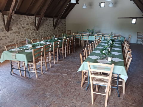 Lange tafels met groene tafelkleden en bloemstukken in een rustieke zaal bij Domaine Papillon, Occitanië, Frankrijk.