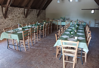 Lange tafels met groene tafelkleden en bloemstukken in een rustieke zaal bij Domaine Papillon, Occitanië, Frankrijk.