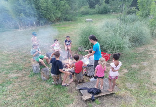 Kinderen en volwassenen rond een kampvuur in Domaine Papillon, een vakantiepark in Occitanië, Frankrijk.