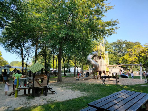 Parco giochi ombreggiato con scivolo e altalene presso Camping les Rives de Grand Lieu, Francia.