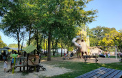 Parco giochi ombreggiato con scivolo e altalene presso Camping les Rives de Grand Lieu, Francia.