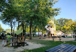 Playground with slides and swings in a shady area at Camping les Rives de Grand Lieu holiday park in France.