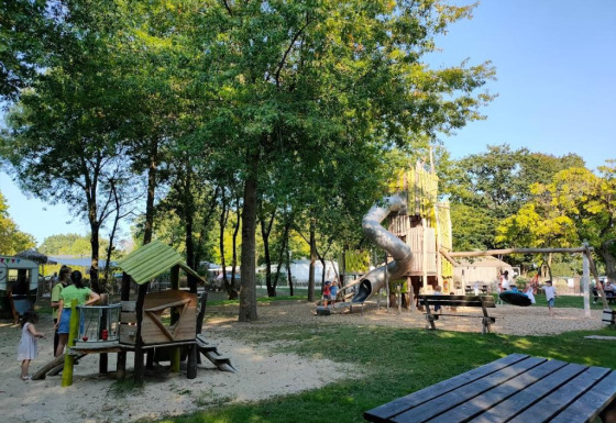 Parco giochi ombreggiato con scivolo e altalene presso Camping les Rives de Grand Lieu, Francia.