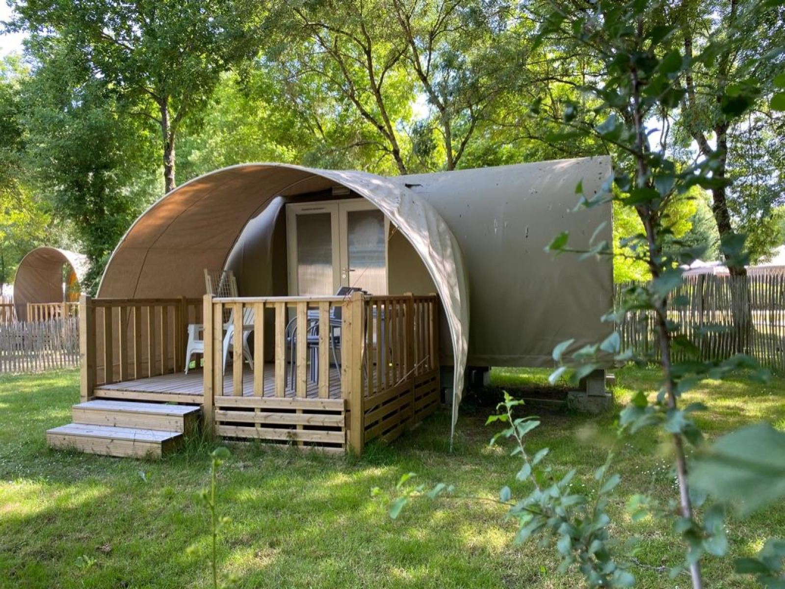 Een Coco Sweet safaritent met houten veranda, omgeven door gras en bomen op een rustige camping.