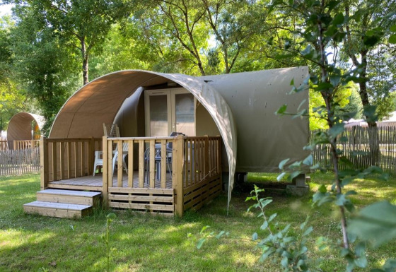 Tenda safari Coco Sweet con veranda in legno, circondata da erba verde e alberi in un campeggio tranquillo.