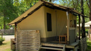 Tenda safari Lodge Balearic con veranda in legno, circondata da alberi e natura in una giornata soleggiata.