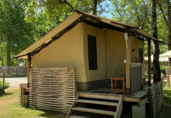 Tenda safari Lodge Balearic con veranda in legno, circondata da alberi e natura in una giornata soleggiata.