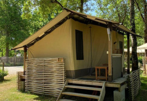 Tenda safari Lodge Balearic con veranda in legno, circondata da alberi e natura in una giornata soleggiata.