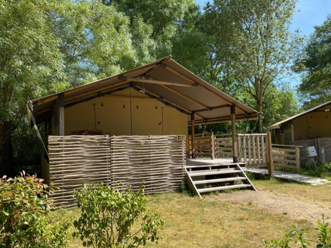 Vista esterna della tenda safari Kenya Lodge con veranda in legno, circondata da alberi e arbusti.