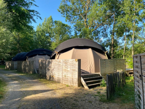 Foto di Transparent Bell Nature house con tende a cupola, recinzioni in legno e alberi sullo sfondo.