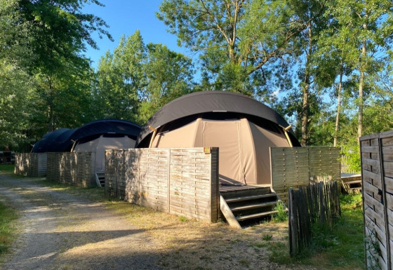 Foto di Transparent Bell Nature house con tende a cupola, recinzioni in legno e alberi sullo sfondo.