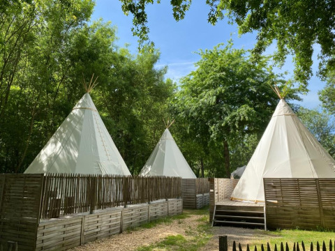 Tre tende tipi circondate da recinzioni in legno e alberi, in una luminosa giornata immersa nella natura.