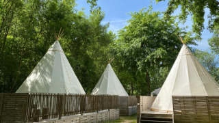 Tre tende tipi circondate da recinzioni in legno e alberi, in una luminosa giornata immersa nella natura.