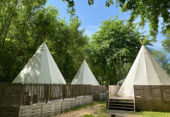 Tre tende tipi circondate da recinzioni in legno e alberi, in una luminosa giornata immersa nella natura.