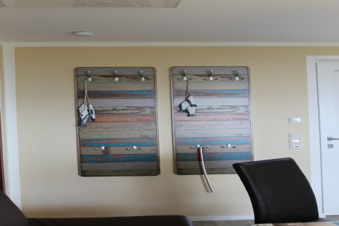 Interieur van lodge Am Strand in Duitsland met kleurrijke kapstokken en zwarte stoelen tegen de muur.