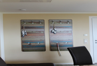 Interieur van lodge Am Strand in Duitsland met kleurrijke kapstokken en zwarte stoelen tegen de muur.