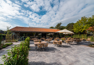 Buitenterras bij Lodge Velthorst op EuroParcs Ruinen, Nederland, met tafels, stoelen en parasols.