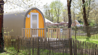 Tenda safari Coco Sweet in un campeggio soleggiato, circondata da una recinzione in legno e alberi verdi.