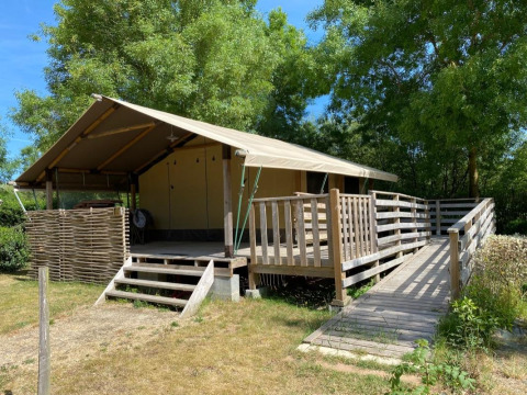 Tenda safari Kenya Lodge con terrazza e rampa in legno al Camping les Rives de Grand Lieu, Francia, in una giornata soleggiata.