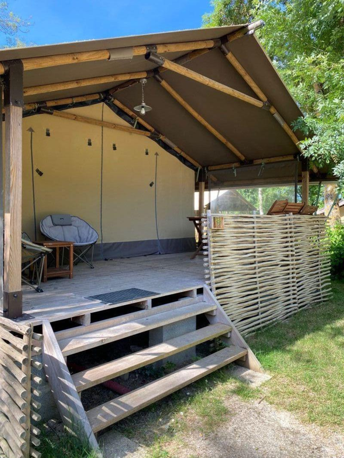 Safari tent Kenya Lodge bij Camping les Rives de Grand Lieu in Frankrijk met houten veranda en zitplek.