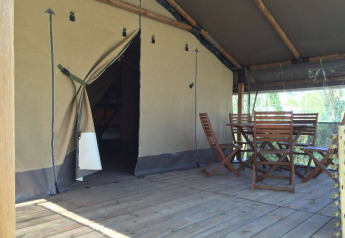 Tenda safari Kenya Lodge al Camping les Rives de Grand Lieu in Francia con veranda in legno e sedie.