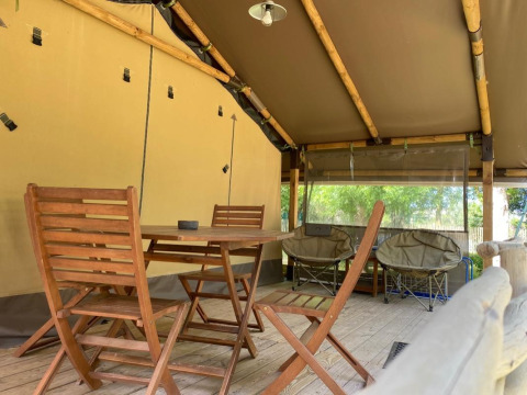 Tenda safari Kenya Lodge al Camping les Rives de Grand Lieu in Francia con mobili e sedie in legno.