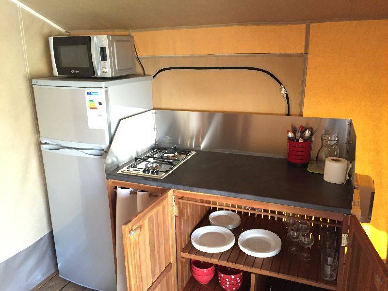 Keukenhoek in de Kenya Lodge safaritent met fornuis, koelkast, magnetron en servies, Frankrijk.