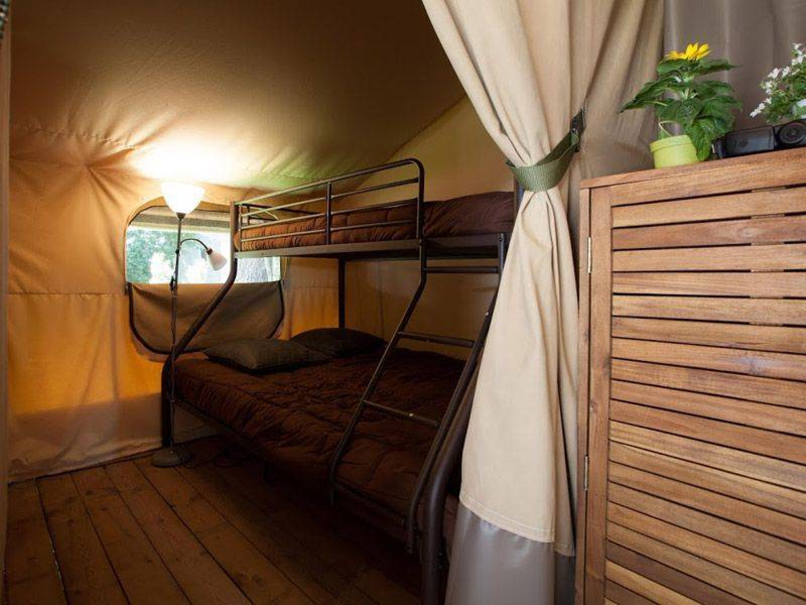 Binnenkant van een safaritent bij Kenya Lodge met stapelbed, houten vloer en planten in Frankrijk.