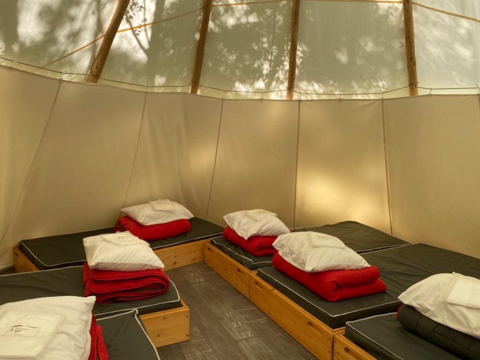 Binnenaanzicht van Tipi Tents bij Camping les Rives de Grand Lieu in Frankrijk met meerdere bedden en rood beddengoed.