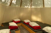 Interno delle Tipi Tents al Camping les Rives de Grand Lieu in Francia, con diversi letti e biancheria rossa.